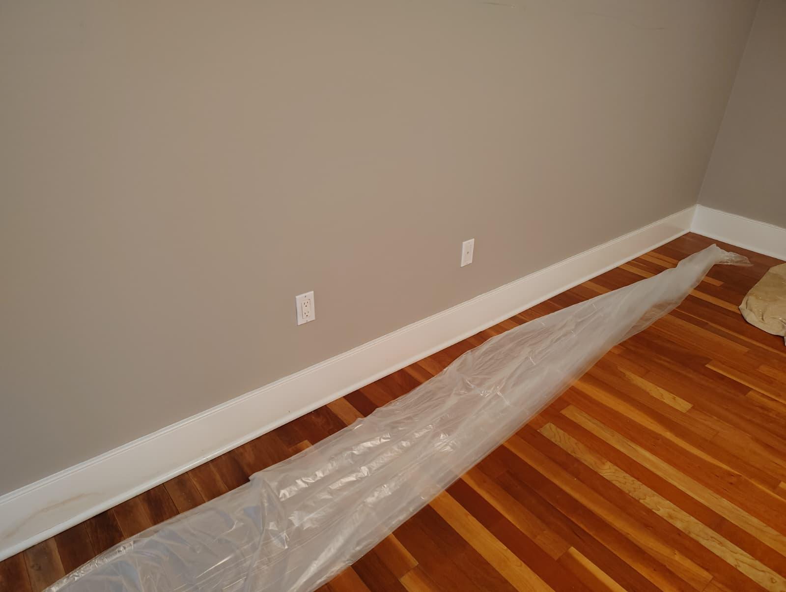 New white baseboard installed and painted along the wall with floor protection in place