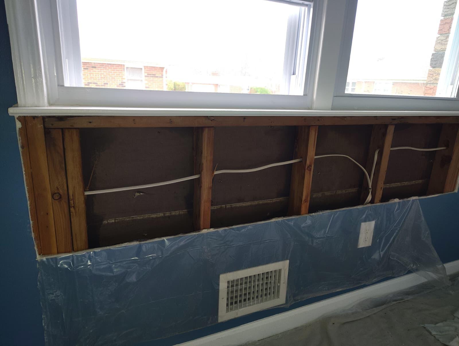 Drywall removed below window exposing studs with mold damage, area contained with plastic sheeting