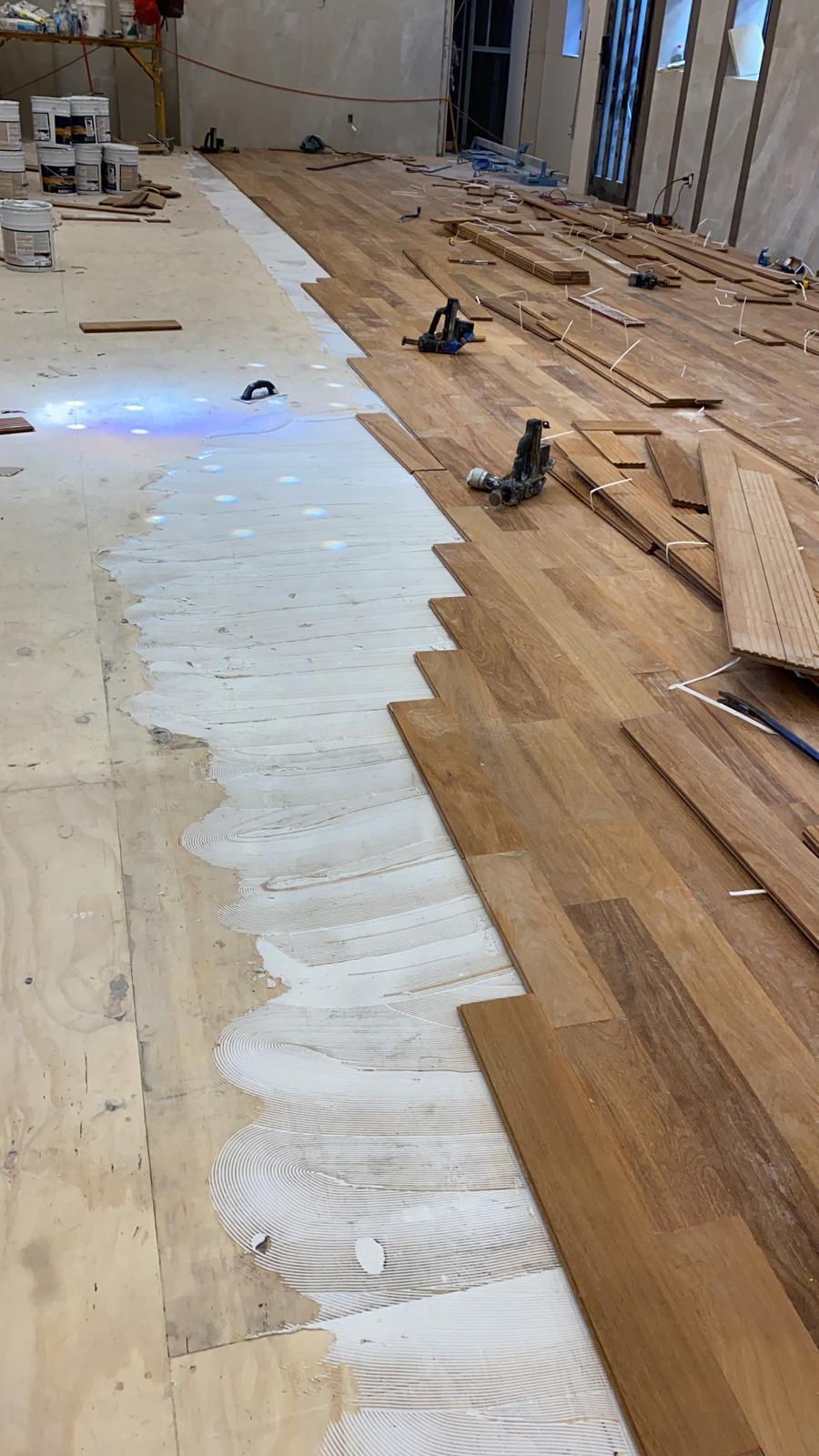 Glue-down installation of solid hardwood planks over the prepared subfloor